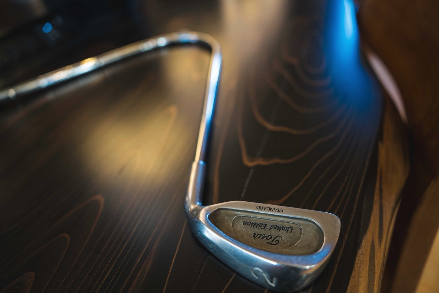 The original clubhead and bent shaft of a vintage iron on a dark wood table