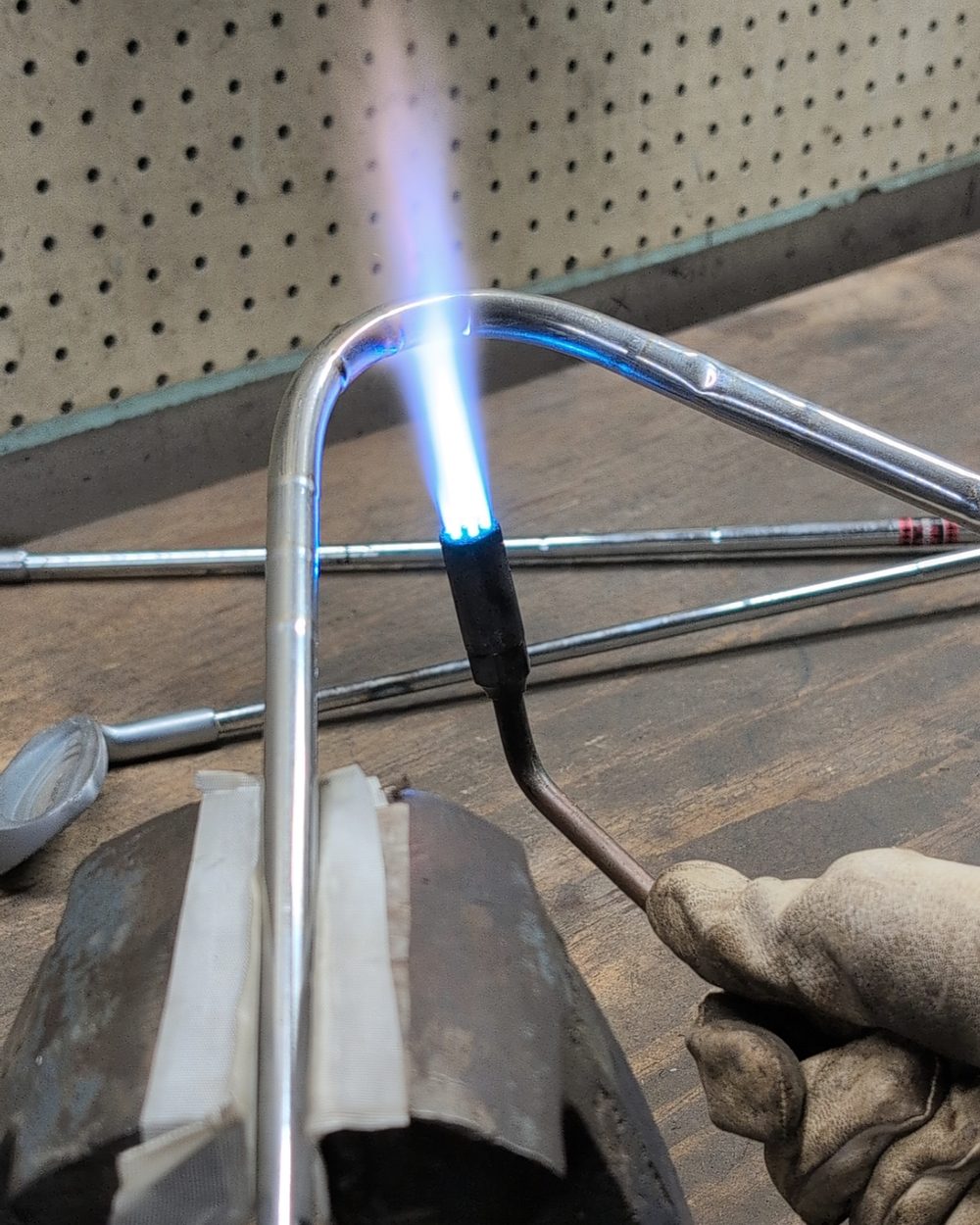 A torch heating a golf shaft bent in a vise in the workshop