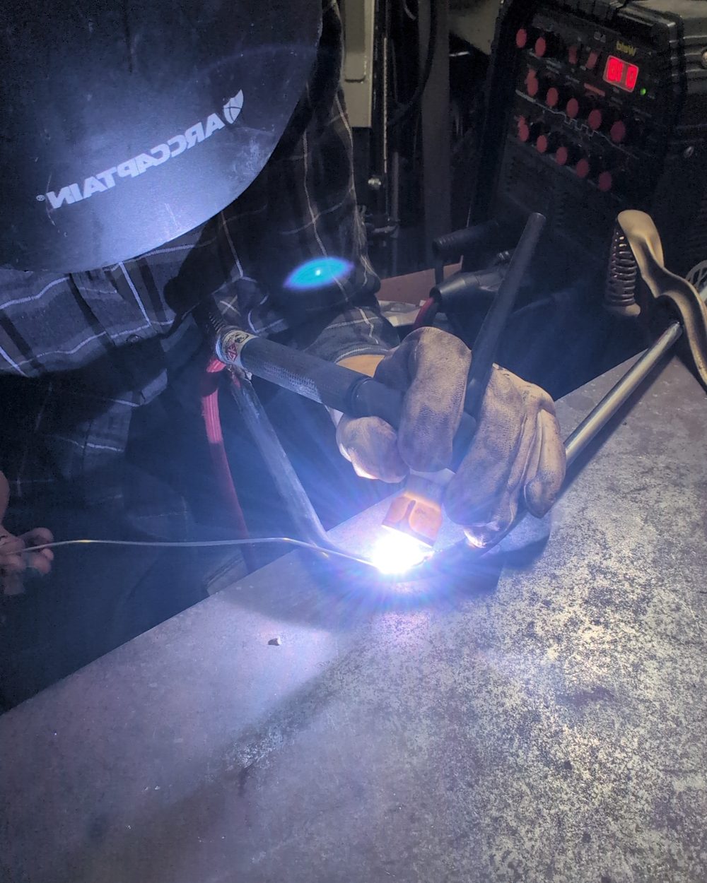 The artist in a welding helmet welding a bent golf iron at the workbench